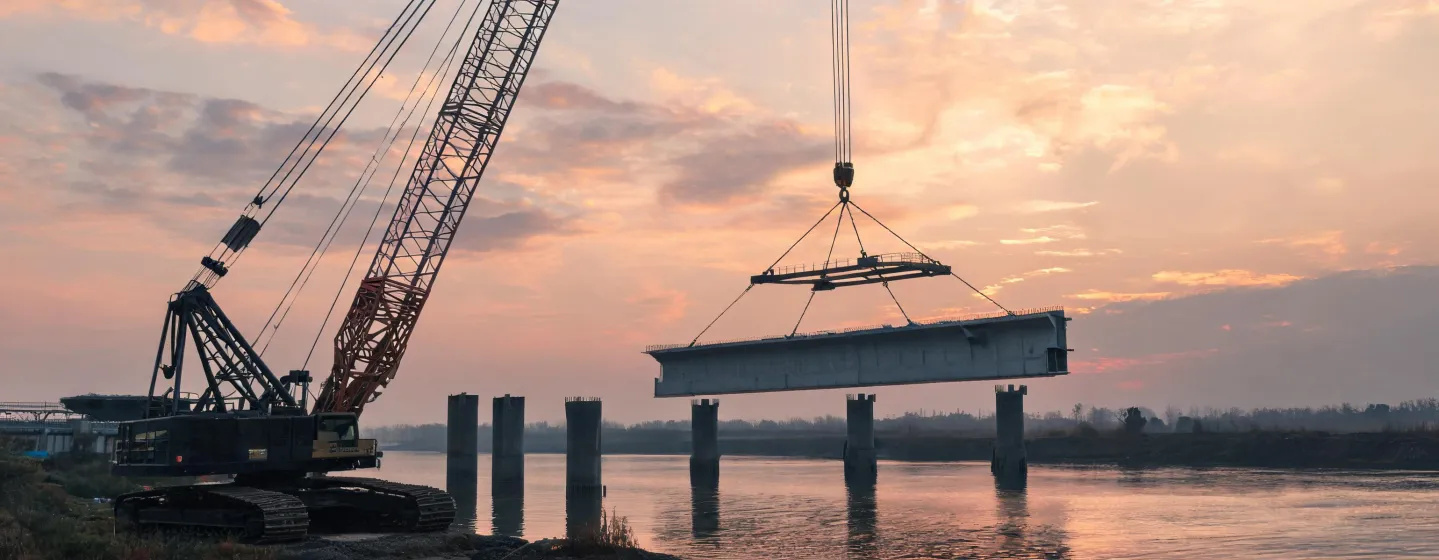 Crawler crane setting precast bridge segments at dusk